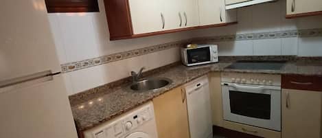 A compact kitchen with a washing machine, a microwave, a sink, and a stove.