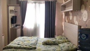 A hotel room with a bed, an air conditioning unit, a water dispenser, and a patterned wall. - DLP Rooms (Central Jakarta)