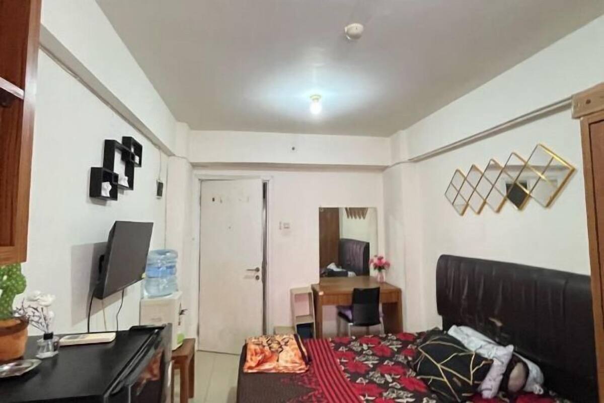 Habitació amb llit, escriptori, cadira, televisió i un dispensador d'aigua.