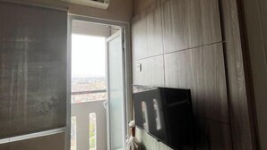 A room with a sliding door leading to a balcony, a mounted flat-screen TV, and an air conditioning unit on the wall. - DLP Rooms (Central Jakarta)