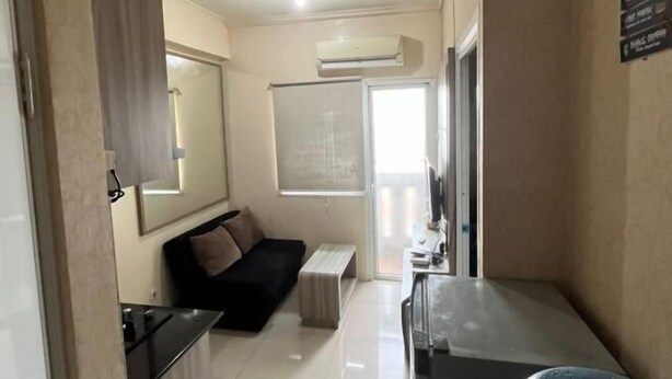 A compact living space with a sofa, a small table, an air conditioning unit, and a sliding door leading to a balcony. - DLP Rooms (Central Jakarta)