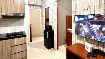 A kitchen with a gas stove, a black refrigerator, and a television on a wooden stand.