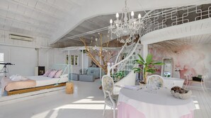 Una habitación amplia con una cama, una mesa de comedor, un candelabro y una escalera.