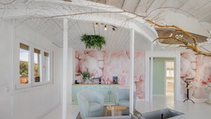 Una habitación amplia con diseño moderno, que incluye un ventanal grande, un rincón de descanso con dos sillones, una mesita y una planta decorativa.