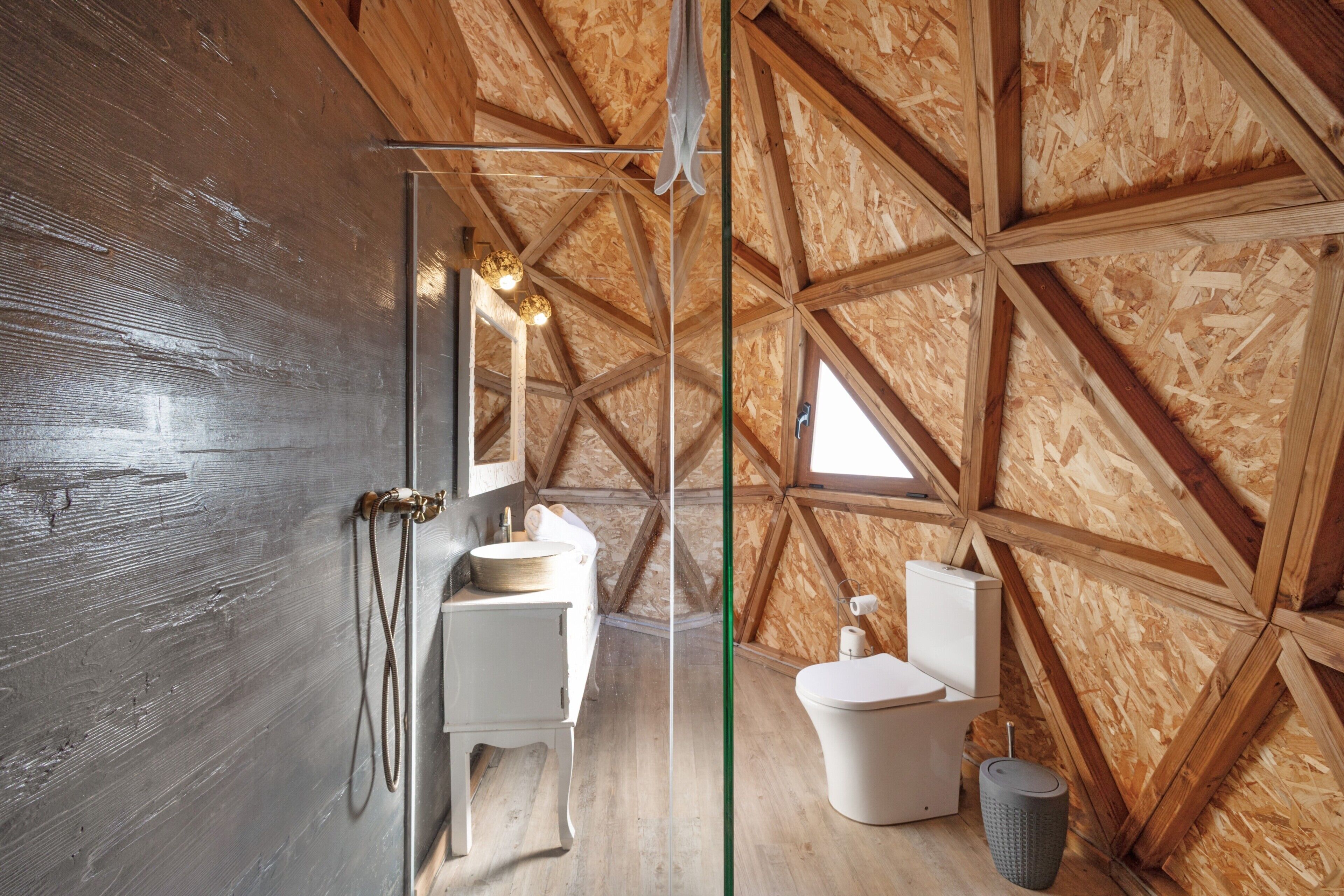 Un intérieur rustique avec des éléments en bois, notamment un plafond en bois, un évier blanc, des toilettes et un espace douche.