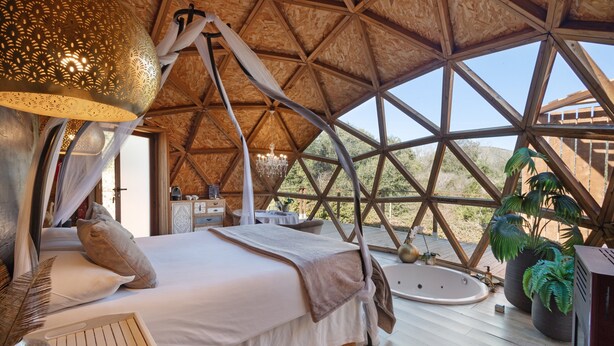 A spacious, high-ceilinged room with a large bed, a bathtub, and a view of the outdoors.