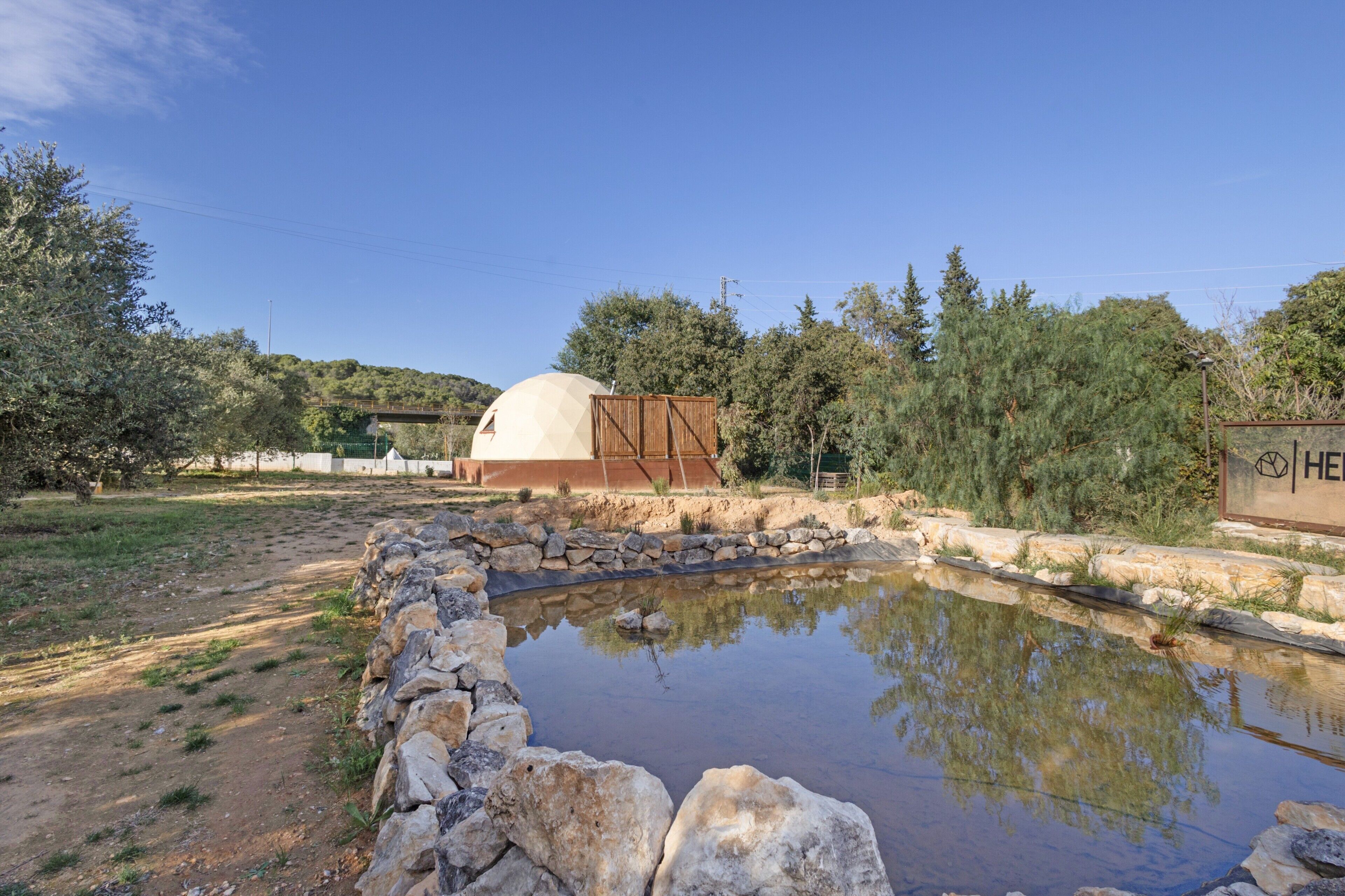 A spherical building with a dome roof, surrounded by a stone wall and a small pond.