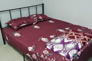 Ein Einzelbett mit Blumenmusterdecke und zwei Kissen, ein Metallkopfteil und eine schlichte Wand.