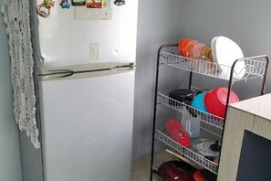 Eine Küche mit Kühlschrank, einem Metallregal mit Geschirr und einer weißen Spitzenwaschlappen an der Wand.