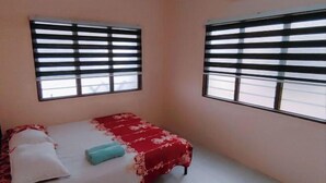 A single bed with a red and white bedspread, two windows with horizontal blinds, and a white wall. - Homestay Che Wan Satu (Kuala Kuantan)