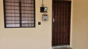 A door with a metal gate, a window with horizontal bars, and a small electrical box on the wall. - Homestay Che Wan Satu (Kuala Kuantan)