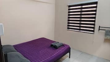 A single bed with a purple bedspread, a window with blinds, and a towel hanging on a rack.