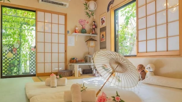Een traditionele Japanse kamer met tatami vloeren, een futon bed, schuifdeuren en uitzicht op groen buiten.