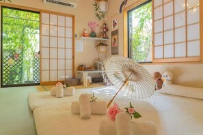 A traditional Japanese-style room with tatami flooring, a futon bed, sliding doors, and a view of greenery outside. - Tokyo Yoshihisa Garden Hotel (Tokyo)