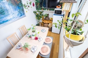 A dining area with a table set for four, surrounded by chairs, with a small refrigerator and a hanging plant. - Tokyo Yoshihisa Garden Hotel (Tokyo)