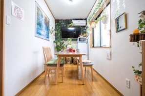 Un petit coin repas avec une table et des chaises en bois, un four à micro-ondes et un téléviseur fixé au mur.