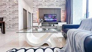 Een moderne woonkamer met een stenen muur, een glazen salontafel, een blauwe bank en een flatscreen televisie op een houten standaard.
