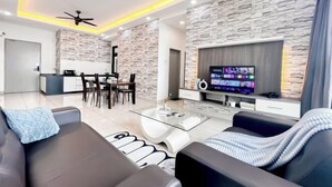 Een moderne woonkamer met een stenen muur, een flatscreen televisie en een eethoek, met een keuken op de achtergrond.