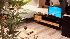 Une chambre à coucher confortable, aménagée en style loft, avec un lit, un téléviseur posé sur un meuble en bois, une petite table avec un verre de vin et une télécommande.