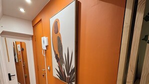 Un couloir avec un mur orange, une porte en bois et un tableau encadré représentant un perroquet.