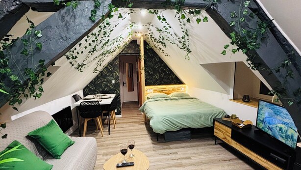 Une chambre confortable située dans les combles, avec un lit, un canapé, une petite table avec des boissons et une télévision.