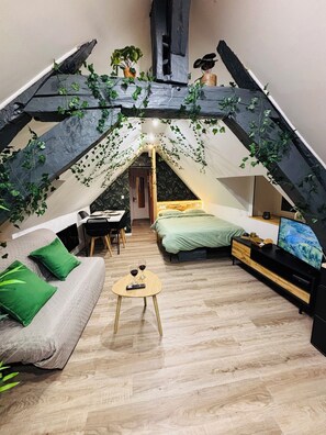 A cozy attic bedroom with a bed, a sofa, a small table with drinks, and a TV.