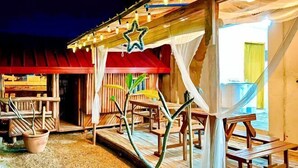 An outdoor dining area with wooden tables and benches, a red awning, and string lights.