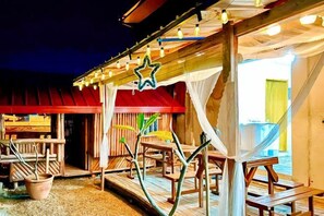A wooden outdoor seating area with tables and chairs, a covered section with a red roof, and a star decoration. - The Lavana Villa Del Matabungkay by RedDoorz (Lian)