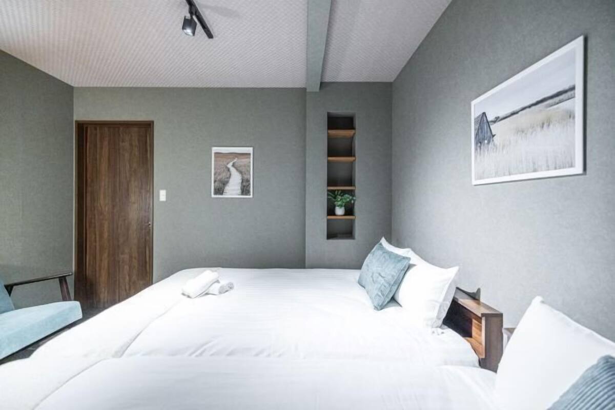 A bedroom with a large bed, a wooden door, a small shelf with a plant, and a framed picture on the wall.