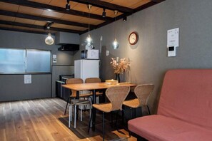Ein Zimmer mit Esstisch, Stühlen, einer Couch, einer Uhr und einem an der Wand befestigten Gerät.