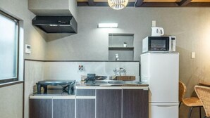 A compact kitchen with a built-in stove, a microwave, and a refrigerator. There is a small dining area with a table and chairs. - Travel time Momotani - 9min walk to Tōgaku Station, 18min walk to Shitennoji Temple (Osaka)