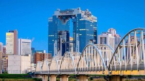 A bridge with a unique arch design over a body of water, with modern buildings in the background. - Travel time Momotani - 9min walk to Tōgaku Station, 18min walk to Shitennoji Temple (Osaka)