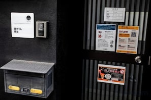 Une porte noire dotée d’un lecteur de cartes, une petite boîte aux lettres et plusieurs panneaux d’information, notamment des codes QR et un panneau interdisant de fumer.