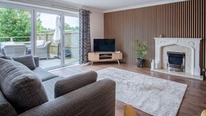 A living room with a sofa, TV, fireplace, and a view of the outdoors. - Ridgeway Meadow Bungalow - 3 Bedroom - Manorbier (Tenby)