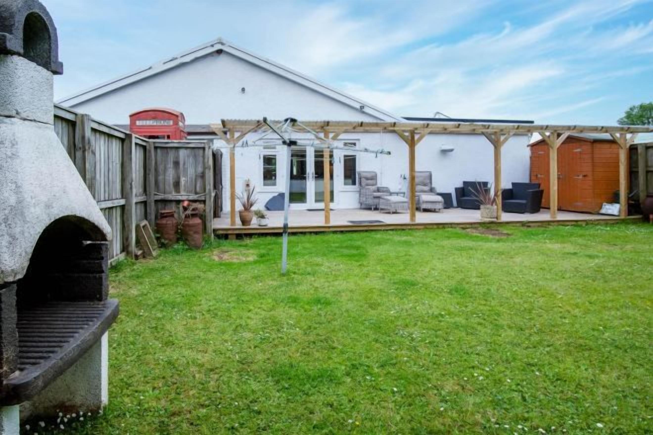 A backyard with a barbecue grill, a wooden fence, and a covered patio area with outdoor furniture.