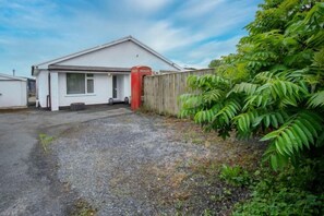 Un bâtiment d’un seul étage, avec un garage, une boîte aux lettres rouge et une allée gravillonnée.