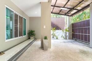 Un espace extérieur abrité doté d’un sol en béton, de plantes en pot, d’une porte-fenêtre coulissante et d’un portail en métal.