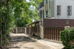 A residential street with a gated entrance, a building with a garage, and a tree-lined pathway.