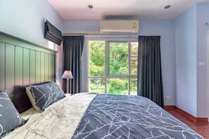 Ein Schlafzimmer mit Bett, Fenster mit Vorhängen, Klimaanlage und Lampe.