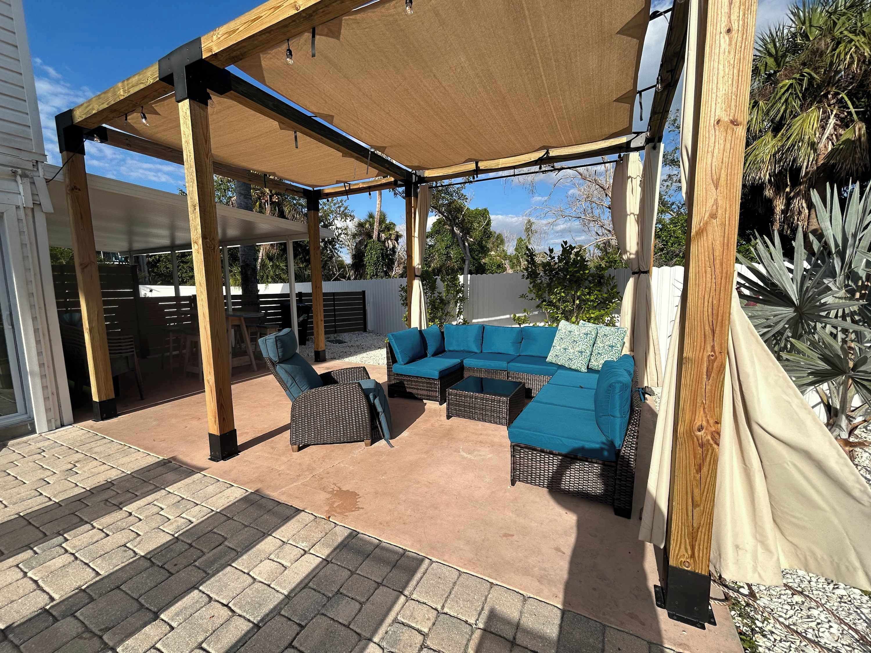 A covered patio with a sectional sofa, wicker chairs, and a table.