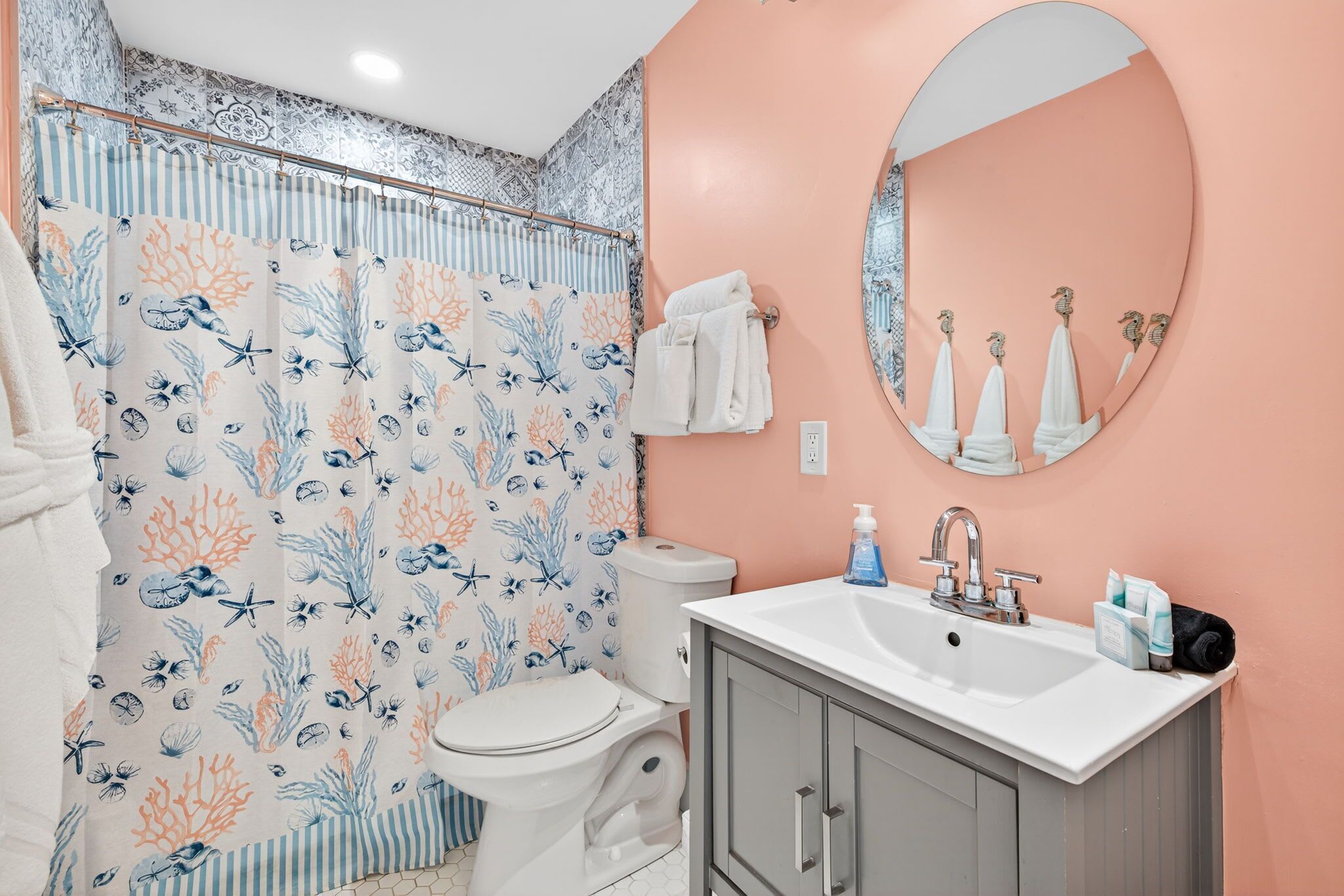 A bathroom with a toilet, sink, and shower curtain with a marine theme.