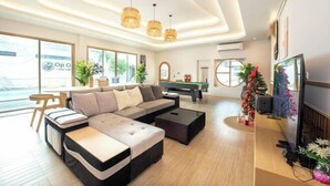 A modern living room with a sectional sofa, a coffee table, and a pool table. There is a TV on the right and a dining area in the background. - De Beach pool villa. New Villa 3 min walk from the beach 5 rooms (Pattaya)