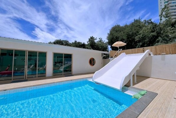 A swimming pool with a slide, a glass-enclosed area, and a wooden deck.