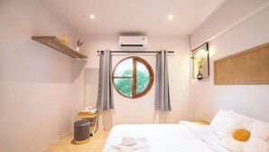 A hotel room with a bed, a round window, a small table with a lamp, and a trash bin. - De Beach pool villa. New Villa 3 min walk from the beach 5 rooms (Pattaya)