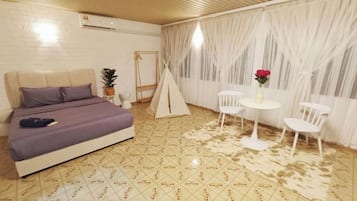 A bedroom with a bed, a small table with chairs, a white curtain, and a tent-like structure.