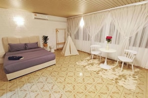 Un dormitorio con una cama, una pequeña mesa con sillas, una cortina blanca y una estructura parecida a una tienda de campaña.