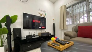 Ein Wohnzimmer mit einem an der Wand befestigten Flachbildfernseher, einer schwarzen Unterhaltungsecke, einem beigefarbenen Sofa mit einem roten Kissen und einem Fenster mit Vorhängen.