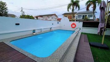A swimming pool with a white wall, a wooden deck, and a grassy area.