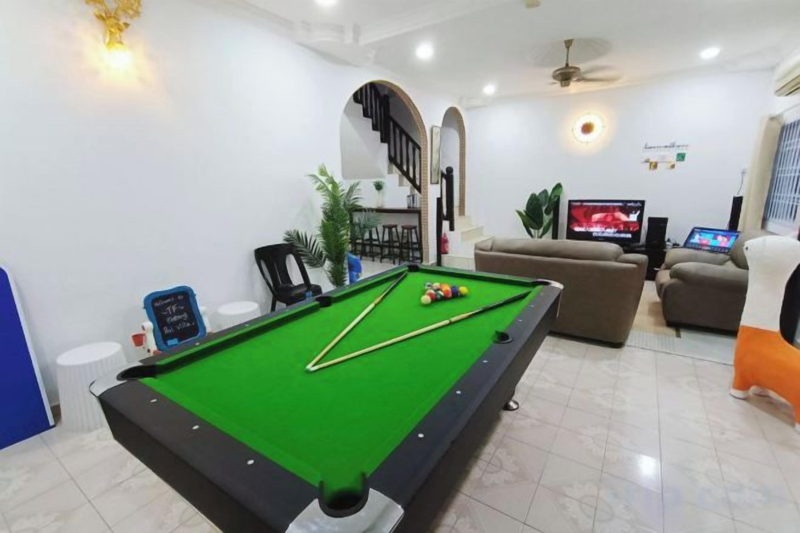 Una mesa de billar en una habitación con televisión, un sofá y una escalera.