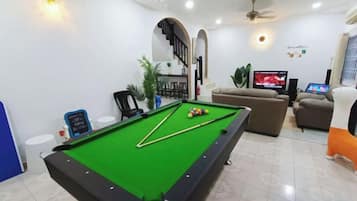 Una mesa de billar en una habitación con televisión, un sofá y una escalera.